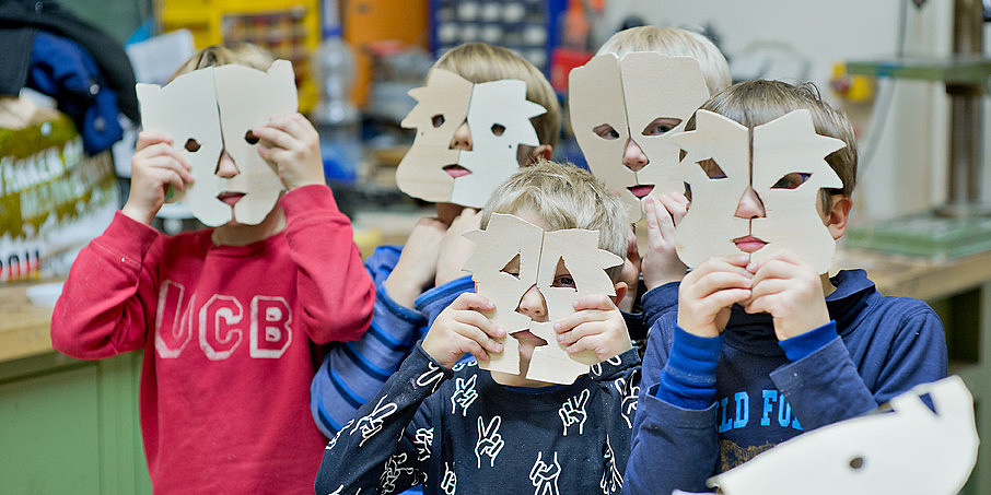 Kinder halten sich Holzmasken vor ihr Gesicht, die als Tiere darstellen. Die Holzmasken haben sie selbst gesägt.