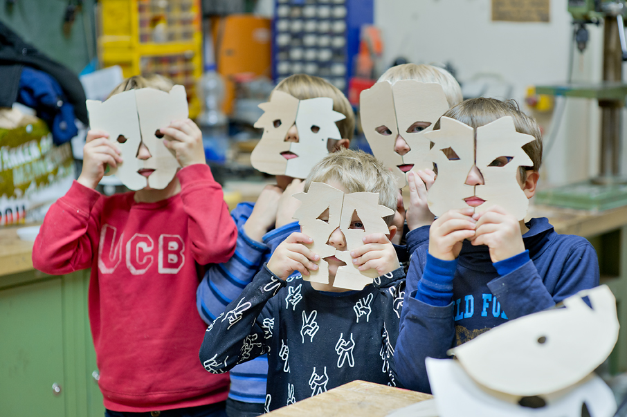 Kinder halten sich Holzmasken vor ihr Gesicht, die als Tiere darstellen. Die Holzmasken haben sie selbst gesägt.